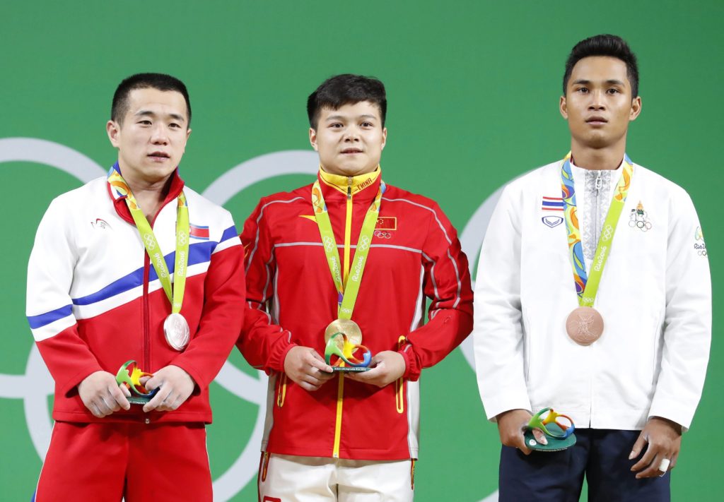 Rio de Janeiro, 2016. augusztus 7. Az aranyérmes kínai Lung Csing-csüan (k), az ezüstérmes ésazk-koreai Om Jun Csol (b) és a bronzérmes thaiföldi Sinphet Kruaithong a 2016-os riói nyári olimpia férfi súlyemelõk 56 kilogrammos versenyének eredményhirdetésén a Rio de Janeiró-i Riocentróban 2016. augusztus 7-én. (MTI/EPA/Nic Bothma)